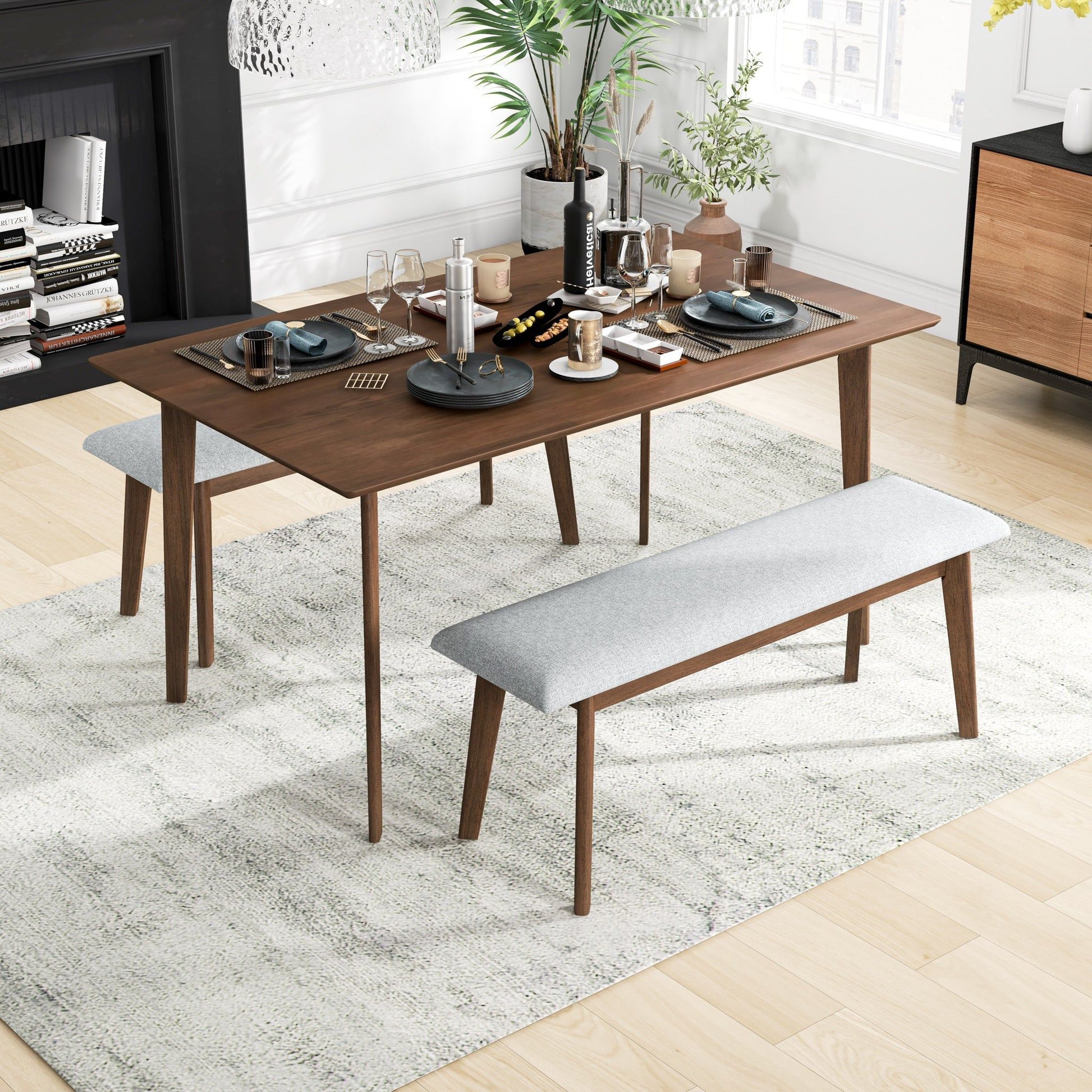 A modern dining room features the Carlos - Dining Table set for four with two benches, light gray cushions, tableware, drinks, and snacks on a light textured rug, illuminated by natural light.