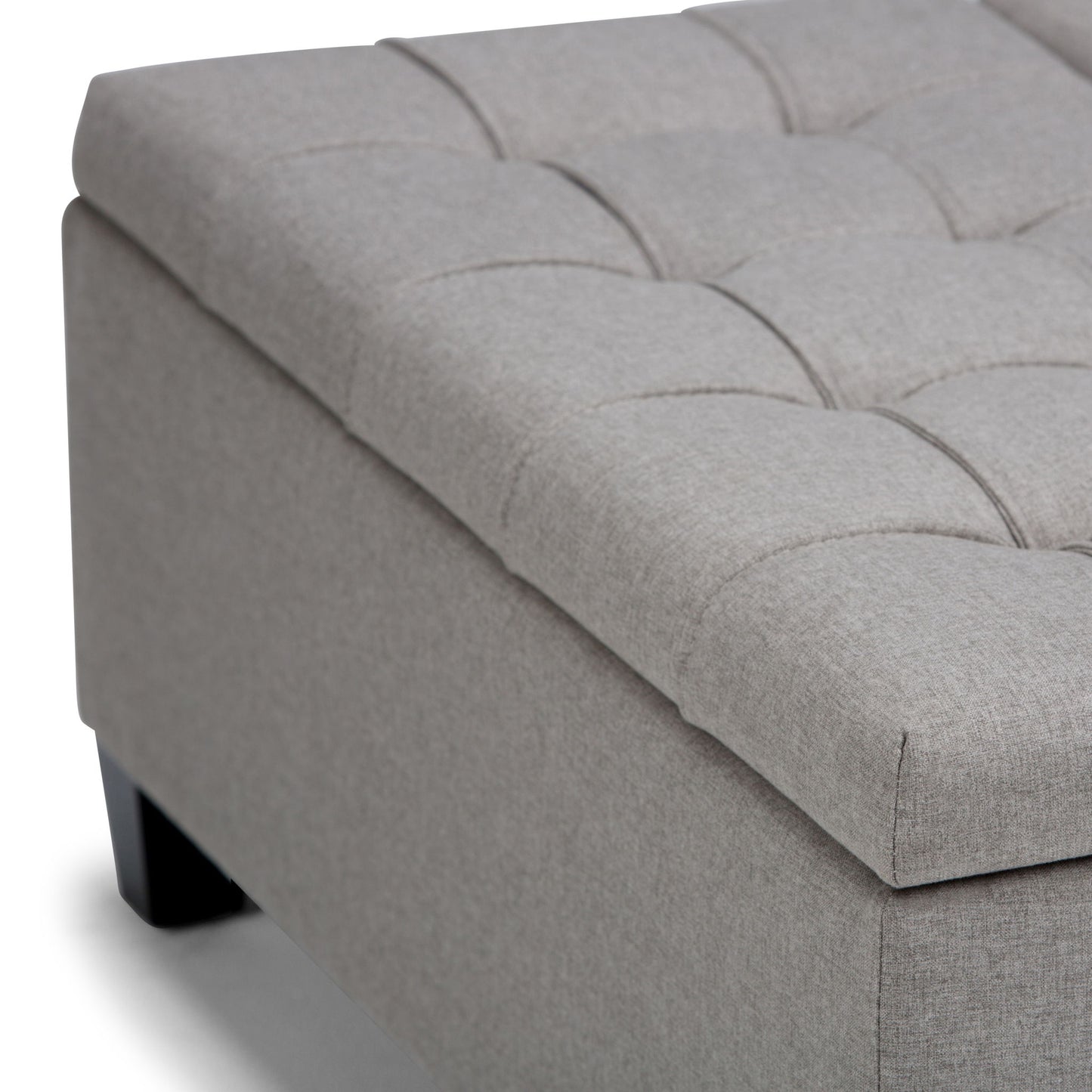 Close-up of the Harrison Upholstered Coffee Table Storage Ottoman featuring a light gray tufted cushion top and dark wooden legs, shown on a white background.