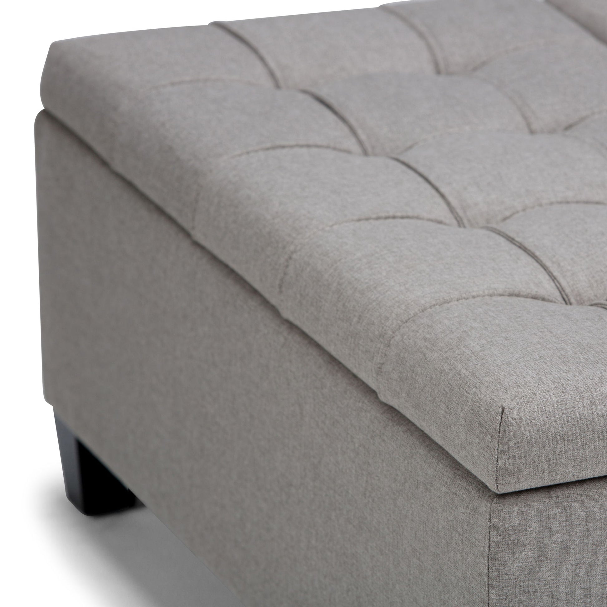 Close-up of the Harrison Upholstered Coffee Table Storage Ottoman featuring a light gray tufted cushion top and dark wooden legs, shown on a white background.