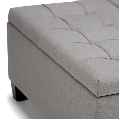 Close-up of the Harrison Upholstered Coffee Table Storage Ottoman featuring a light gray tufted cushion top and dark wooden legs, shown on a white background.
