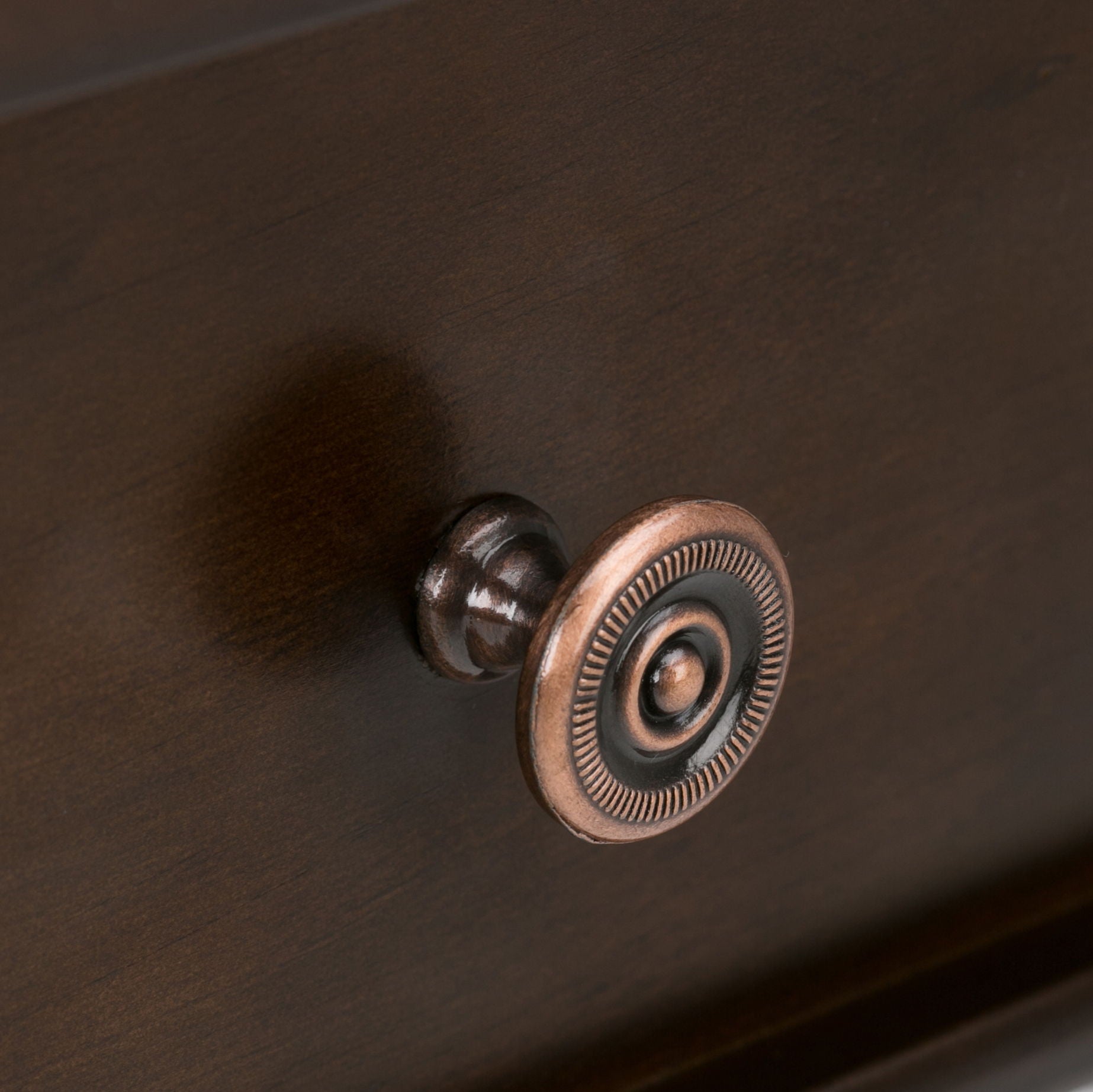 Close-up of a bronze round decorative drawer knob with a ridged edge, mounted on the Carlton Console Sofa Table in Dark Tobacco Brown. The knob casts a soft shadow on the table’s wood surface.