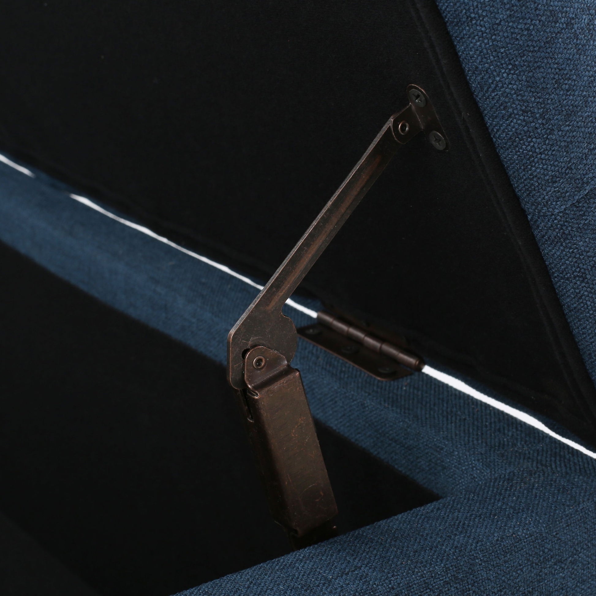 A close-up of the metal hinge inside the Glouster Contemporary Storage Ottoman with button tufting, showing its blue upholstery and partially open lid revealing the interior.