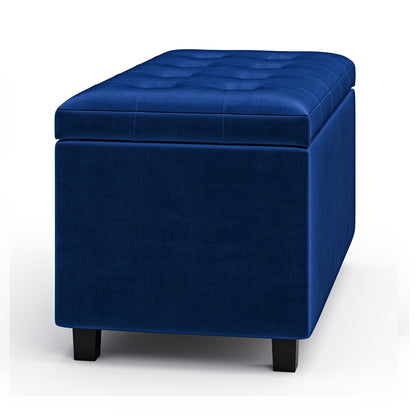 The Cosmopolitan Upholstered Storage Ottoman is rectangular, blue velvet with tufted top detailing and short black legs, shown against a white background.