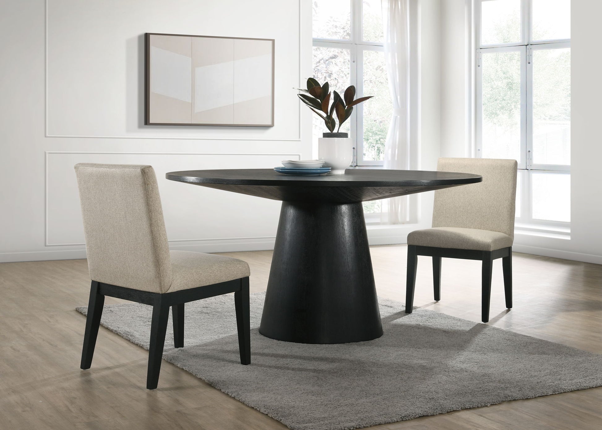 Create a modern dining area with the Jasper Wide Contemporary Round Dining Table and fabric chairs set, featuring beige chairs, a black table, gray rug, potted plant centerpiece, minimalist artwork, and large sunlit windows.
