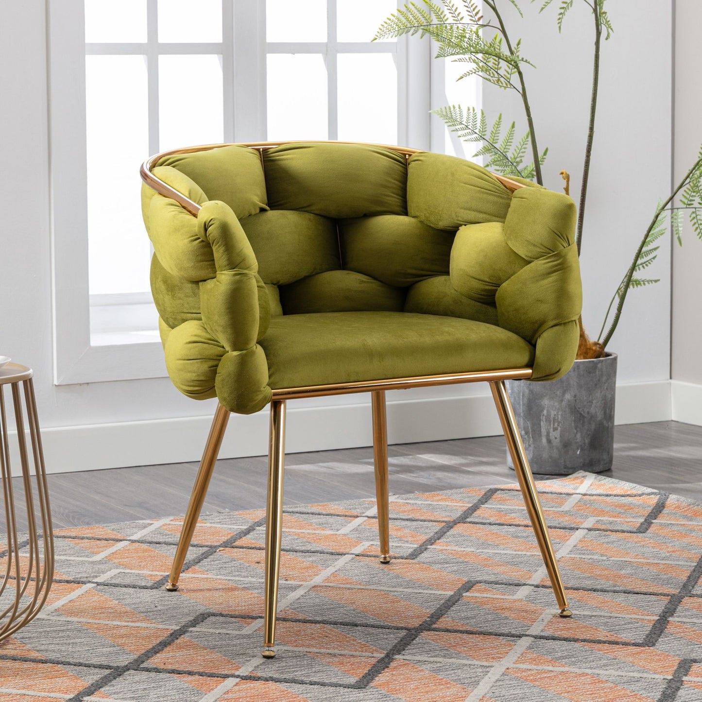 The Luxury Modern Simple Leisure Velvet Single Sofa Chair, featuring a tufted green design and gold metal legs, adds a stylish touch on a geometric rug by the window and potted plant in a bright room.