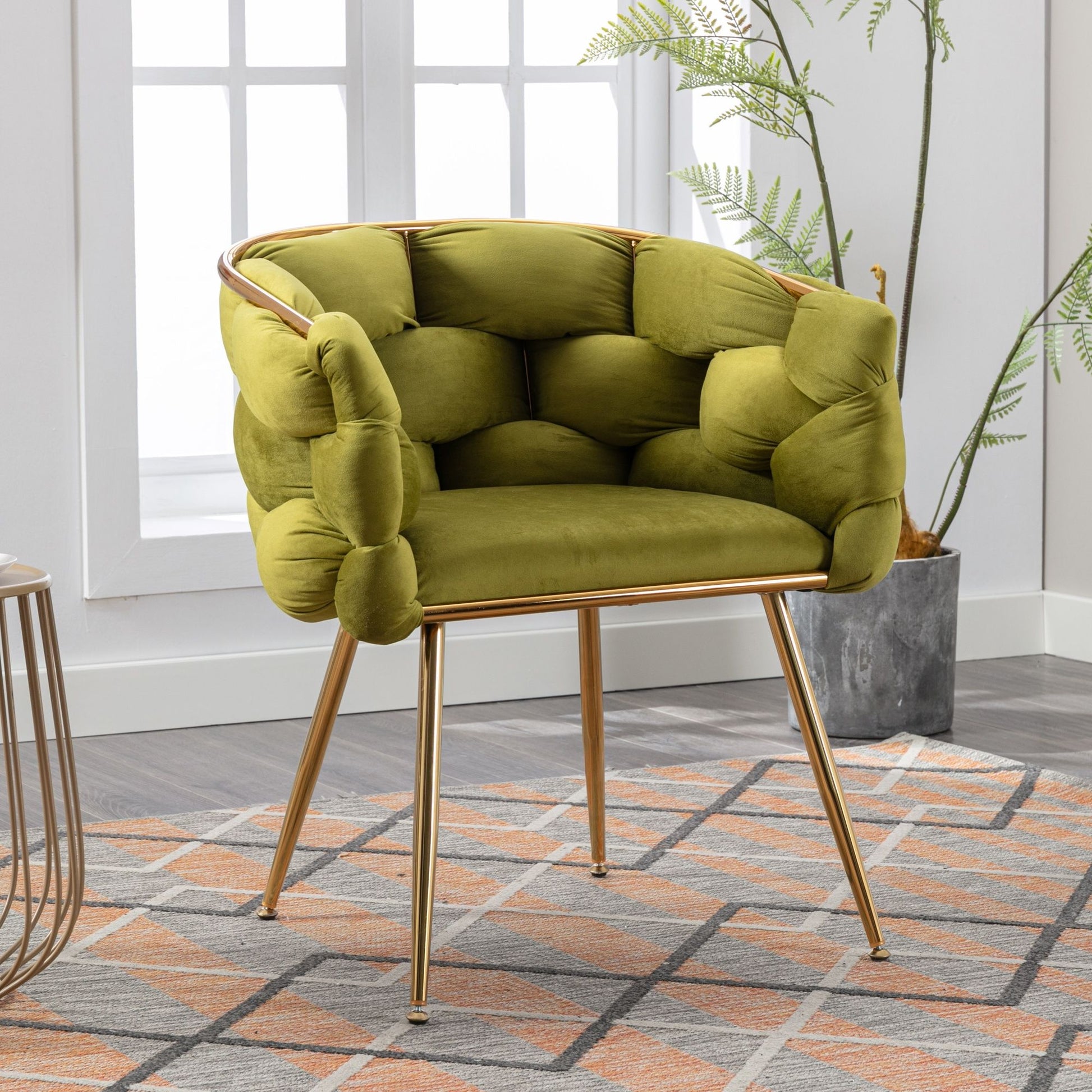 The Luxury Modern Simple Leisure Velvet Single Sofa Chair, featuring a tufted green design and gold metal legs, adds a stylish touch on a geometric rug by the window and potted plant in a bright room.
