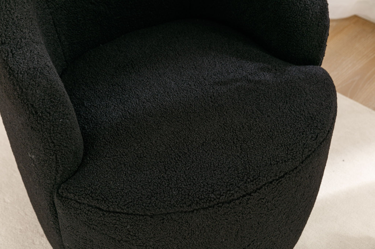 Close-up of the Teddy Fabric Swivel Accent Armchair Barrel Chair, featuring black textured upholstery, curved armrests, a rounded seat, and a powder-coated metal ring base on a light-colored floor.