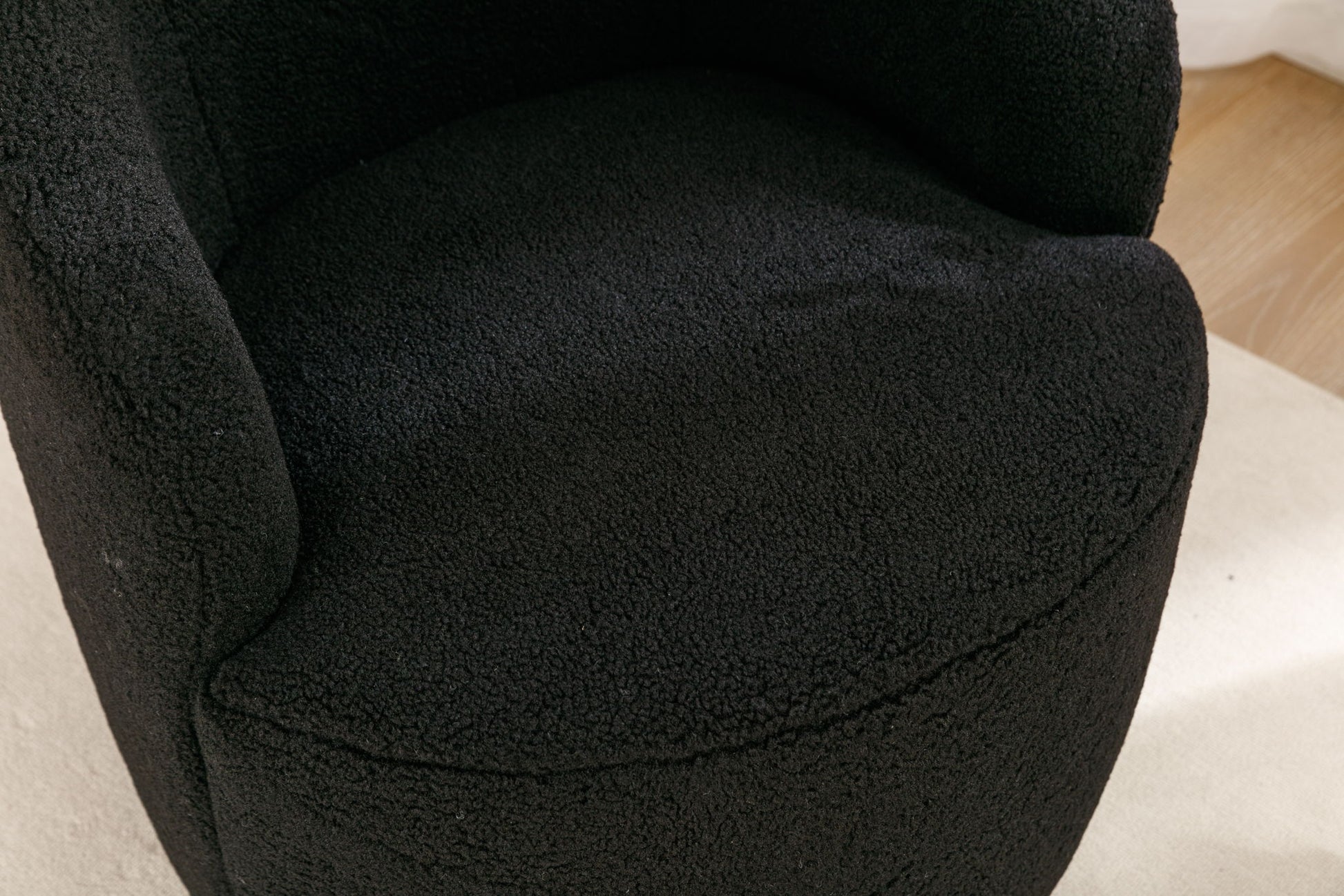 Close-up of the Teddy Fabric Swivel Accent Armchair Barrel Chair, featuring black textured upholstery, curved armrests, a rounded seat, and a powder-coated metal ring base on a light-colored floor.