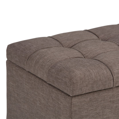 Close-up of the Sienna - Upholstered Storage Ottoman Bench shows its brown, textured fabric with visible stitching and a tufted, cushioned top.