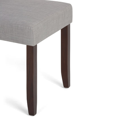 A close-up of the Acadian - Upholstered Parson Dining Chair (Set of 2) shows its light gray upholstered seat and dark wooden legs against a white background.