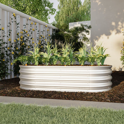 The Heavy Duty Galvanized Raised Garden Bed Kit for Vegetables, Flowers & Herbs is shown in a modern backyard, its white corrugated metal frame filled with green plants and surrounded by flowering vines, trees, and light walls.