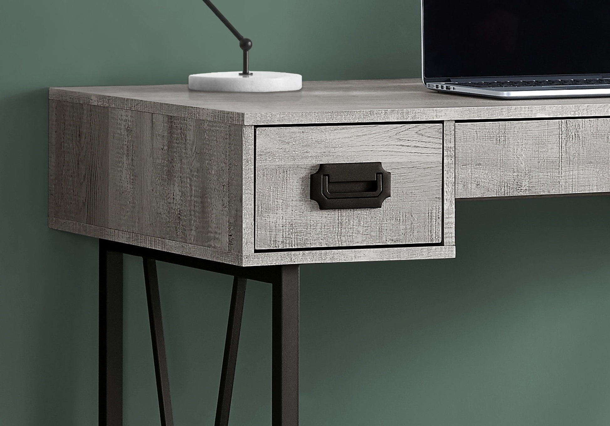 A close-up of the Computer Desk For Home Office, Transitional style with gray wood, black metal frame, storage drawers with black handles, a white lamp, and a laptop on top. The desk is set against a green wall.