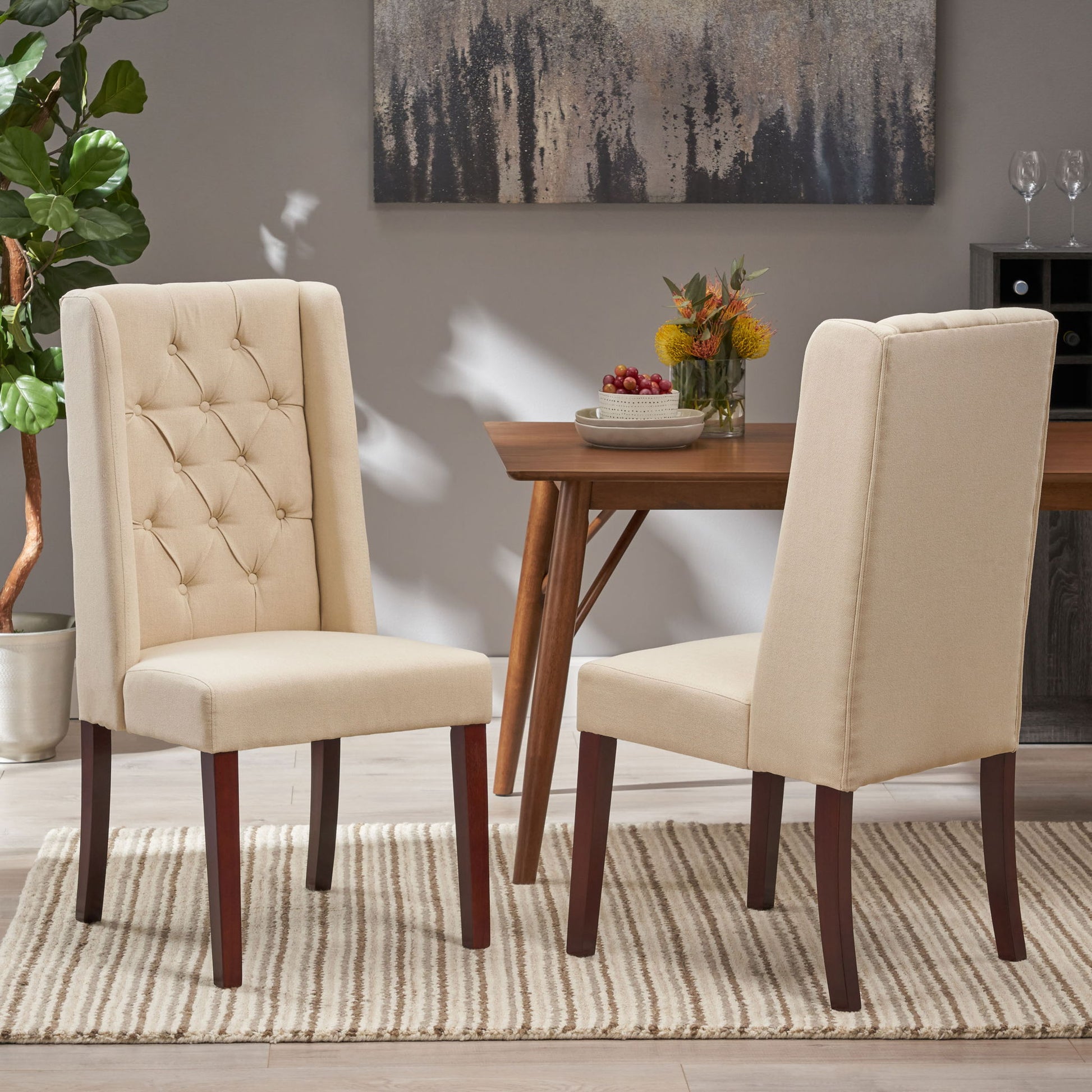 Two Sophisticated Tufted Dining Chairs With High Back Design in beige sit on a striped rug in a modern dining room, paired with a wooden table, decorative plant, and wall art in the background.