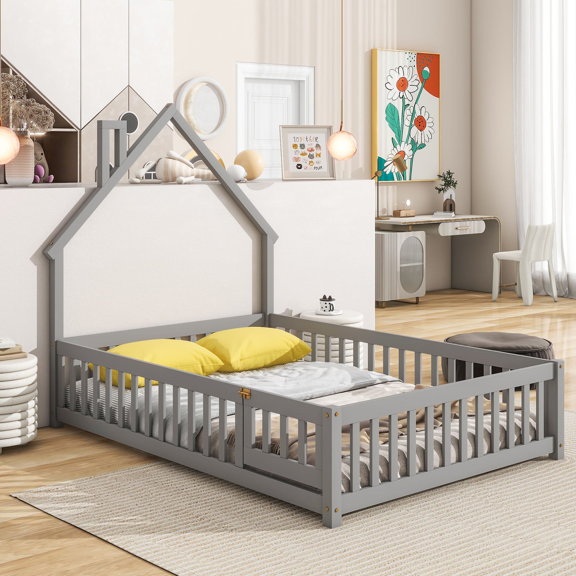 A modern kids’ room featuring the House-Shaped Headboard Floor Bed With Fence in gray, complemented by yellow and gray pillows, wooden flooring, playful decor, kids’ artwork, and a small desk in the background.