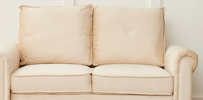 The Graceful Design Plush Comfort Loveseat, a beige two-seater with plush cushions and rolled arms, is set against a plain white wall.