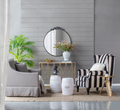 A modern living room with a gray sofa, striped armchair, gold console table, white stools, neutral décor, and a Classic Design Mirror with Baroque inspired frame leaning against the wall on a woven rug.