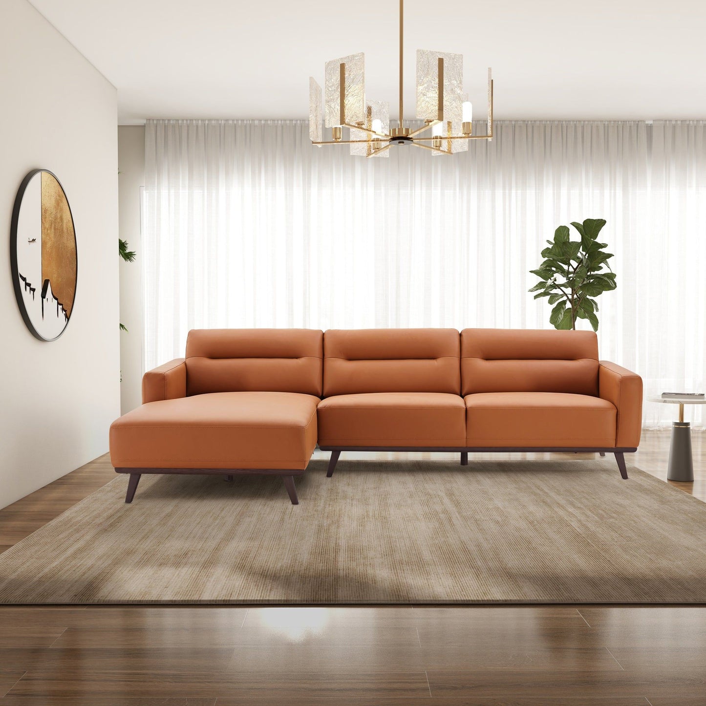 A modern living room featuring the Ella - L-Shaped Sectional Couch in tan on a beige rug, with wooden floors, a large plant, sheer white curtains, round wall art, and a gold chandelier.