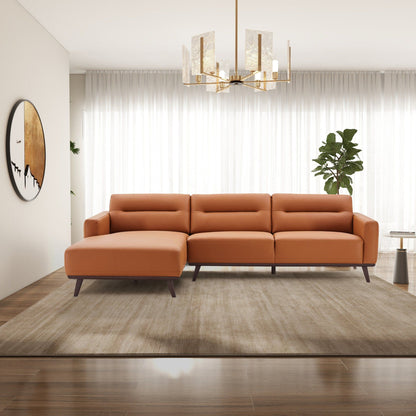 A modern living room featuring the Ella - L-Shaped Sectional Couch in tan on a beige rug, with wooden floors, a large plant, sheer white curtains, round wall art, and a gold chandelier.
