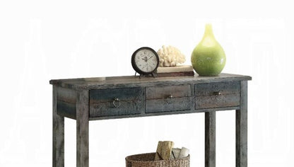 The Glancio - Console Table - Gray features three drawers and a rustic wooden design, topped with a round clock, white coral, and a green vase; a woven basket with rolled-up papers is placed underneath.