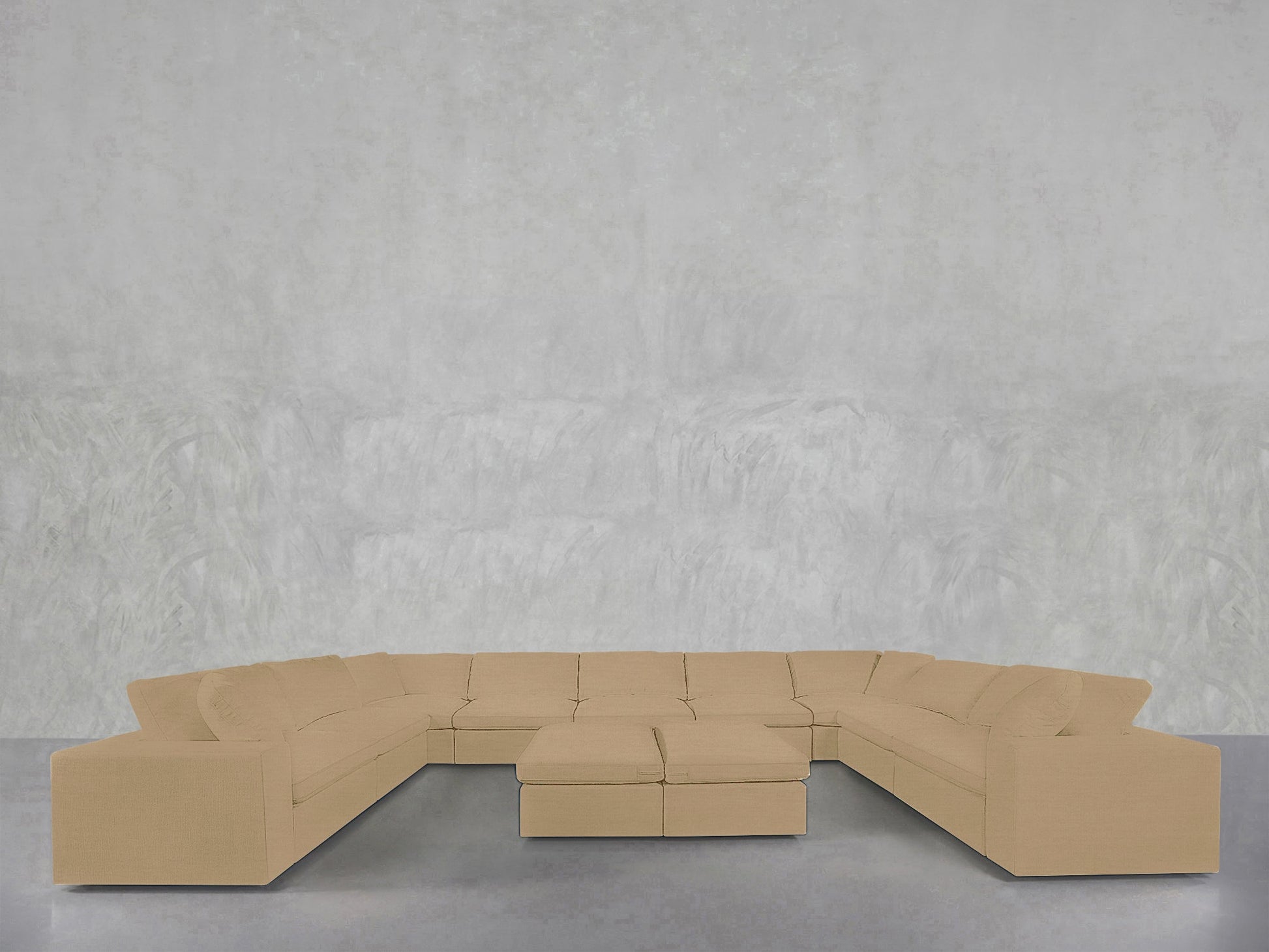 A 9-Seat Modular U-Sectional with Double Ottoman in beige is arranged on a smooth gray floor, set against a textured light gray wall.