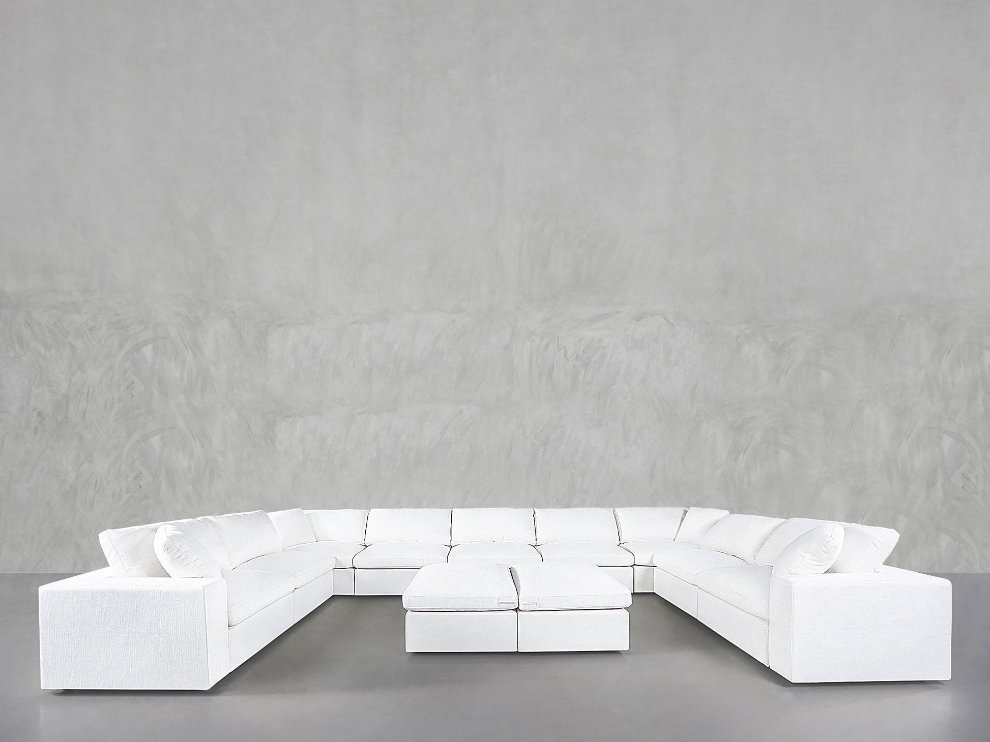 A 9-Seat Modular U-Sectional with Double Ottoman is set in a spacious room featuring smooth, light gray walls and a gray floor.