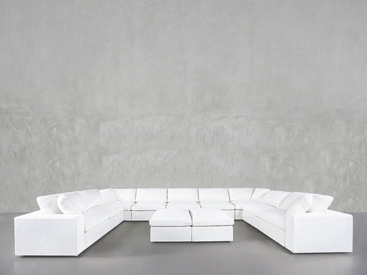 A 9-Seat Modular U-Sectional with Double Ottoman is set in a spacious room featuring smooth, light gray walls and a gray floor.