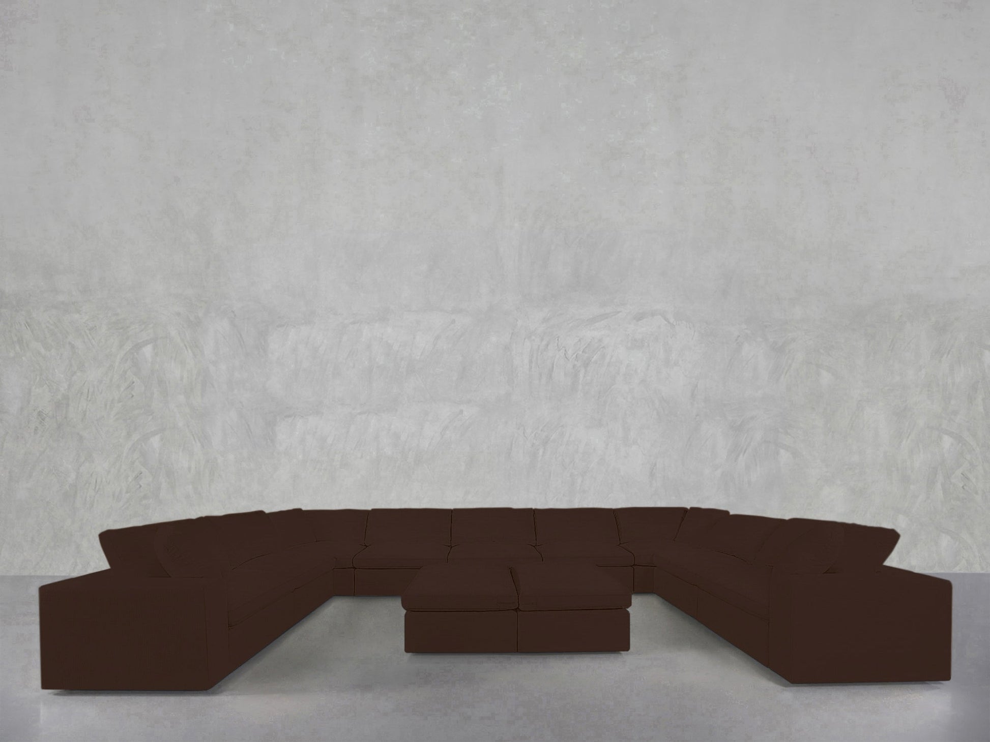 A 9-Seat Modular U-Sectional with Double Ottoman in dark brown sits against a plain light gray textured wall in a minimalist room with a smooth floor.