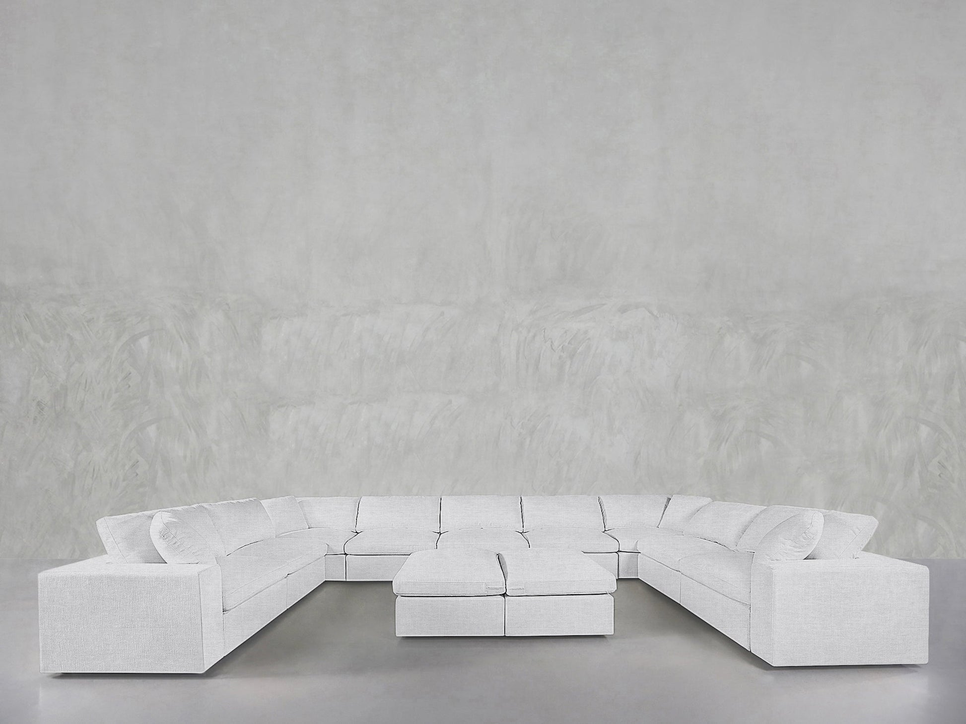 Spacious, modern 9-Seat Modular U-Sectional with Double Ottoman in light gray, displayed against a plain, textured light gray wall and floor.