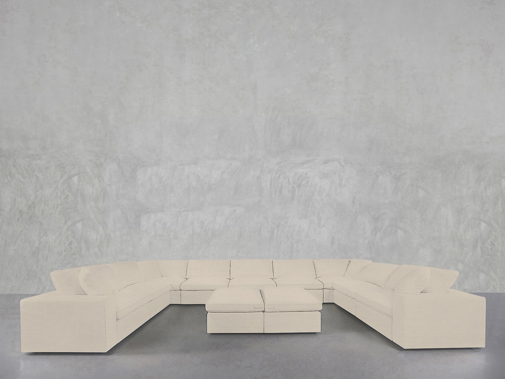 The 9-Seat Modular U-Sectional with Double Ottoman, in light beige, is arranged in a U-shape against a minimalist light gray textured wall and smooth gray floor.