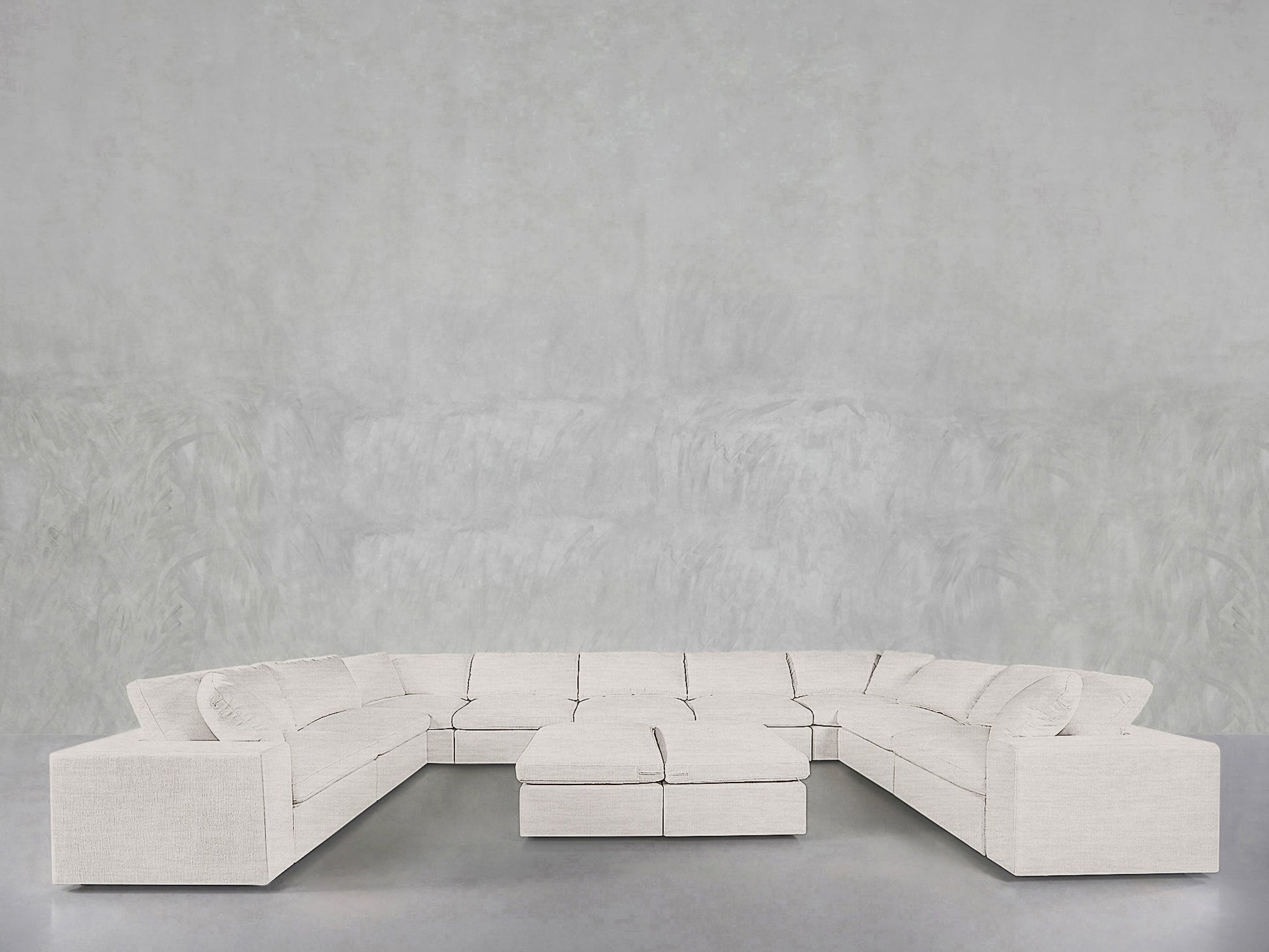 The 9-Seat Modular U-Sectional with Double Ottoman in light beige fabric is arranged around its two matching ottomans, set against a minimalist gray wall and floor.