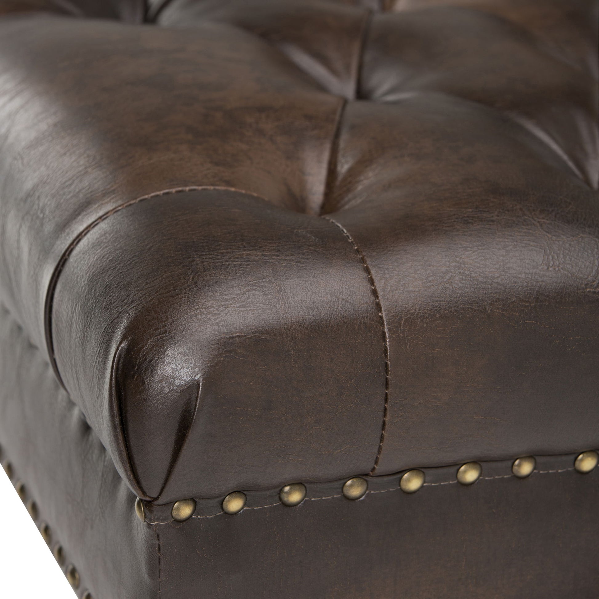 Close-up of the Henley Tufted Ottoman Bench in distressed brown leather, featuring button tufting and brass nailhead trim along the edge. The leather upholstery is smooth with a subtle sheen.