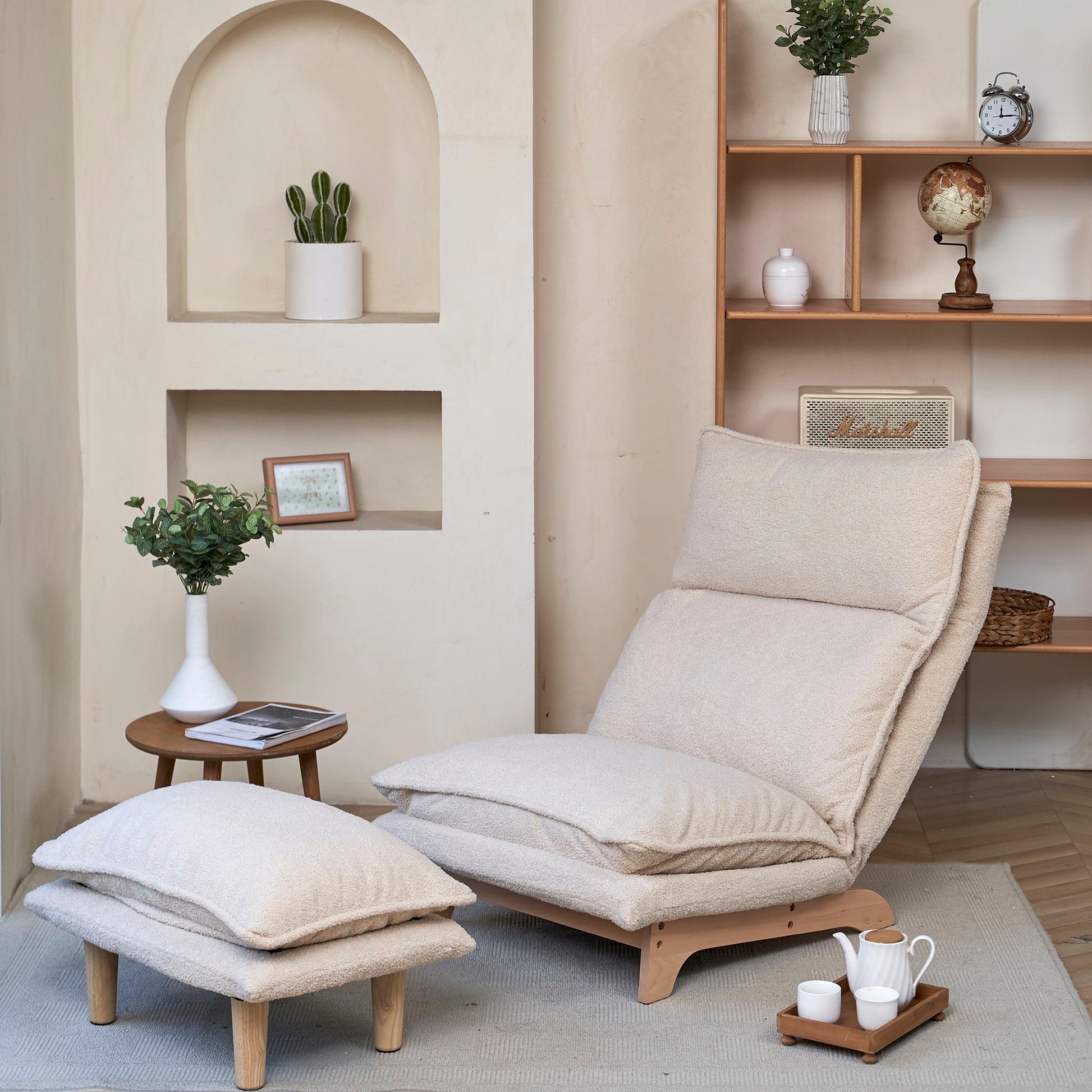 A Single Lazy Sofa Chair Leisure Foldable Reclining Chair in beige with a footrest sits by a small wooden table holding a potted plant and magazines. Nearby, shelves display decor like a globe and framed photo in a softly lit, minimalist room.