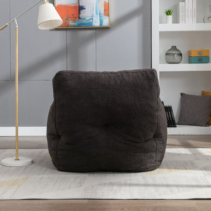 A Soft Teddy Fabric Tufted Foam Bean Bag Chair with teddy fabric in dark gray sits on a light rug in a modern living room, alongside a floor lamp, abstract wall art, and shelves filled with books and decor.