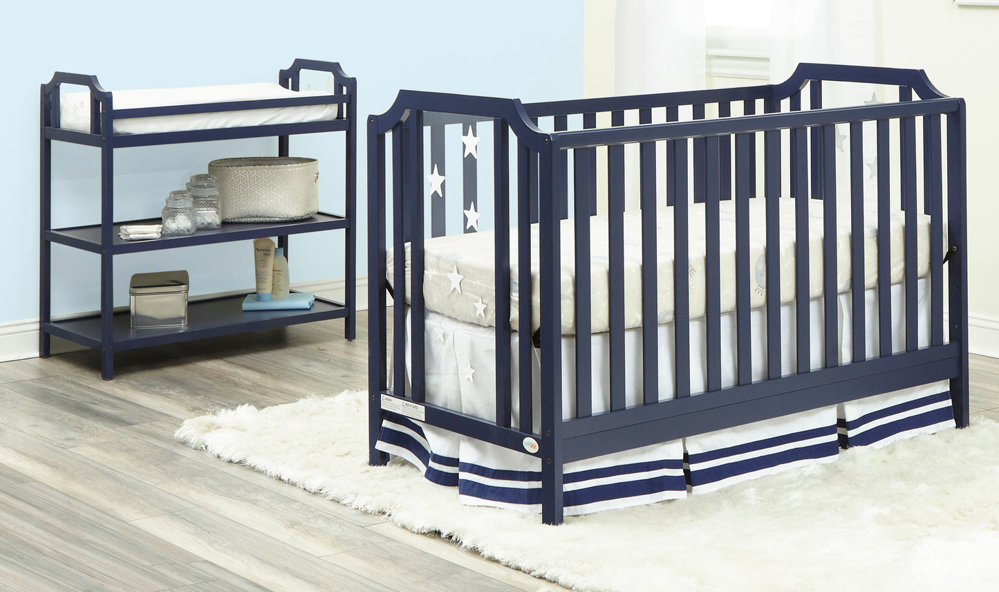 A navy blue crib with star decorations and the Celeste Changing Table with shelves sit on a light wood floor and a white fluffy rug in a bright, softly lit nursery.