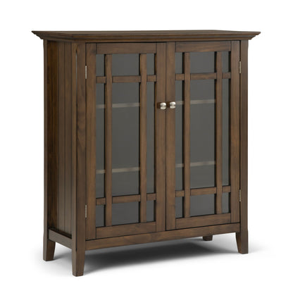 The Bedford Storage Media Cabinet features a dark brown wood finish, two glass-paneled doors with vertical and horizontal accents, silver knobs, and four short legs for a simple, modern look.