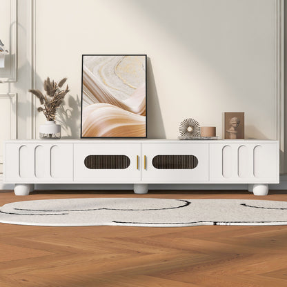A Modern TV Stand for TVs up to 80" with glass door, 2 drawers, cabinets, solid wood legs, and metal handles displays decor like framed art, a vase with dried plants, a sculpture, and an ornament. A white rug sits on the wooden floor.