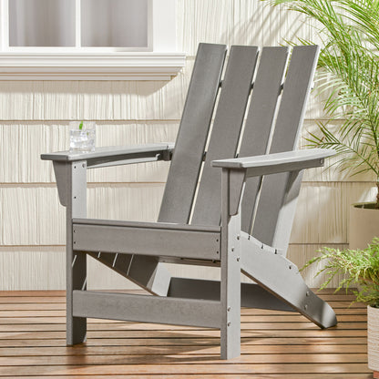 An Enigmara Outdoor High Density Resin Adirondack Chair rests on a wooden deck next to potted plants, holding a clear drink on its armrest, with the house exterior in the background.
