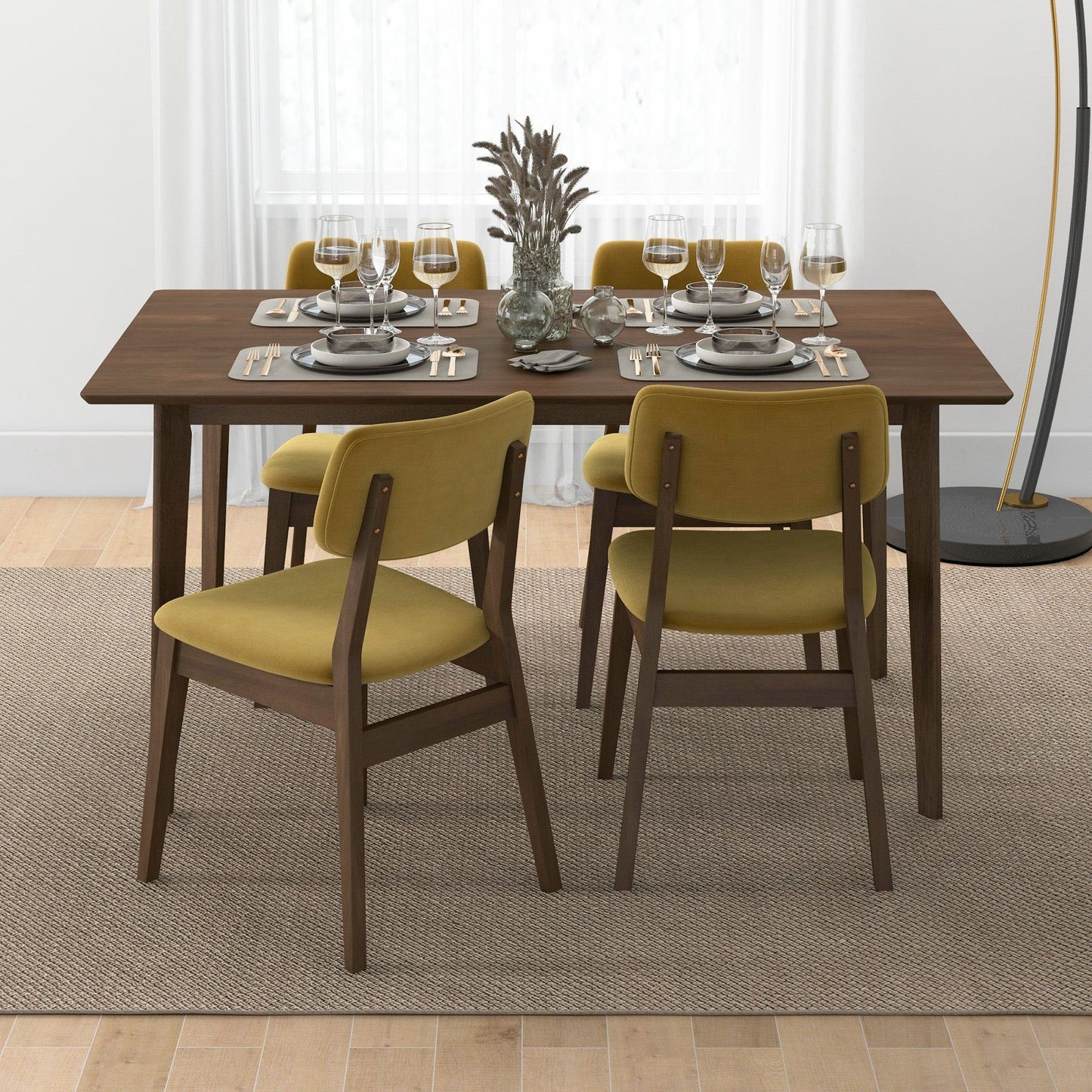 A dark wood dining table set for four with plates, cutlery, wine glasses, and a decorative centerpiece. Four mustard yellow Carlos - Solid Back Side Chairs (two sets of 2) surround the table.