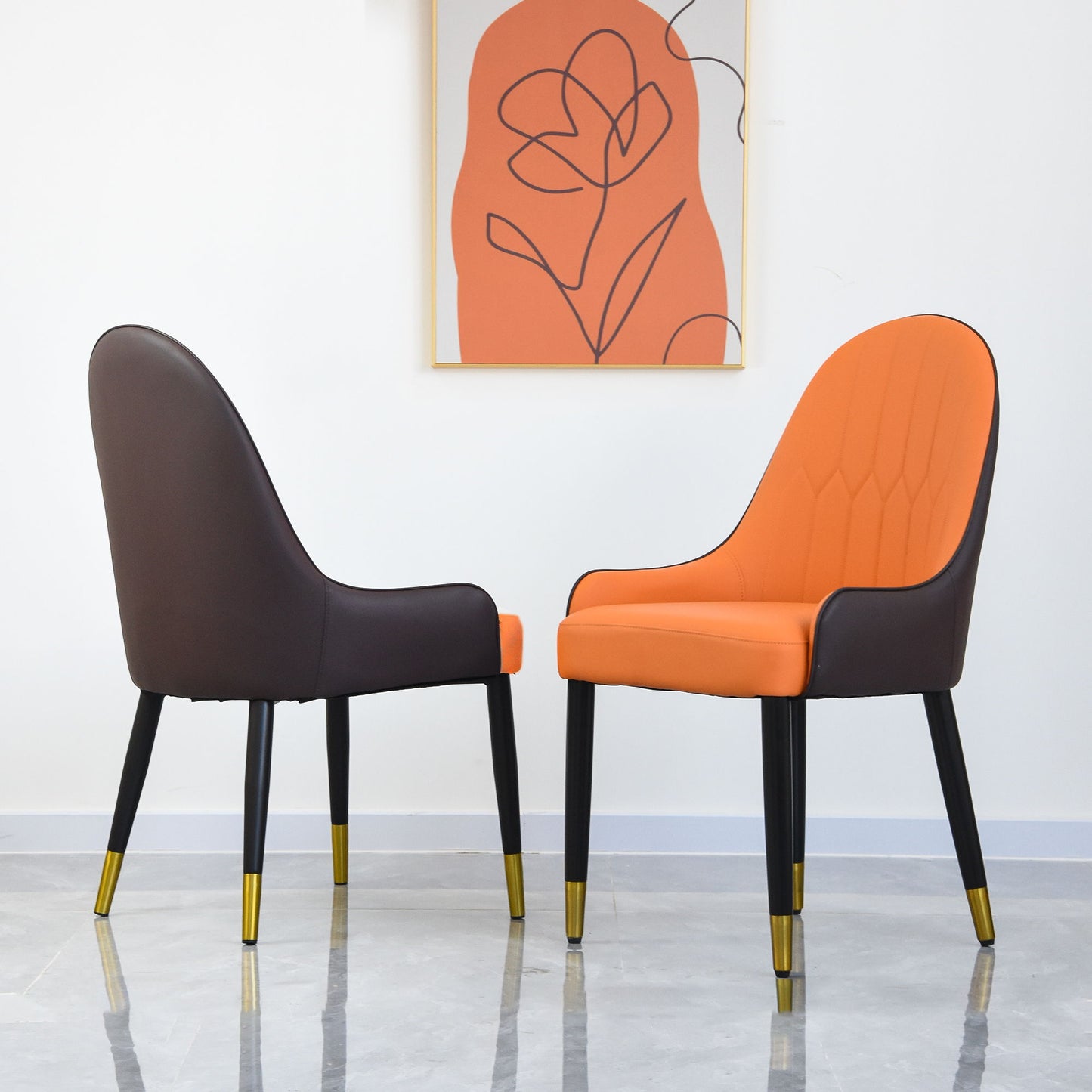 Two Modern PU Sponge-Filled Dining Chairs with solid wood metal legs, ideal for restaurants or living rooms, are set facing each other by a white wall topped with abstract art featuring orange and black lines.
