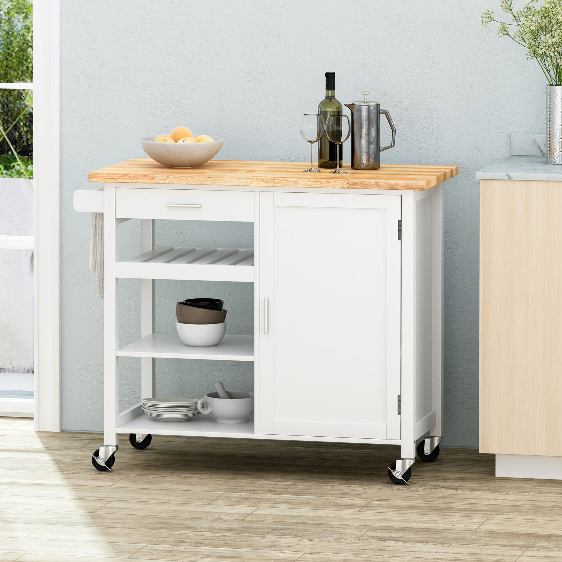 The Contemporary Design Kitchen Cart With Wheels features a white frame, wood countertop, open shelves with bowls, a closed cabinet, and towel bar. On the counter are wine, glasses, a teapot, and a bowl of lemons.