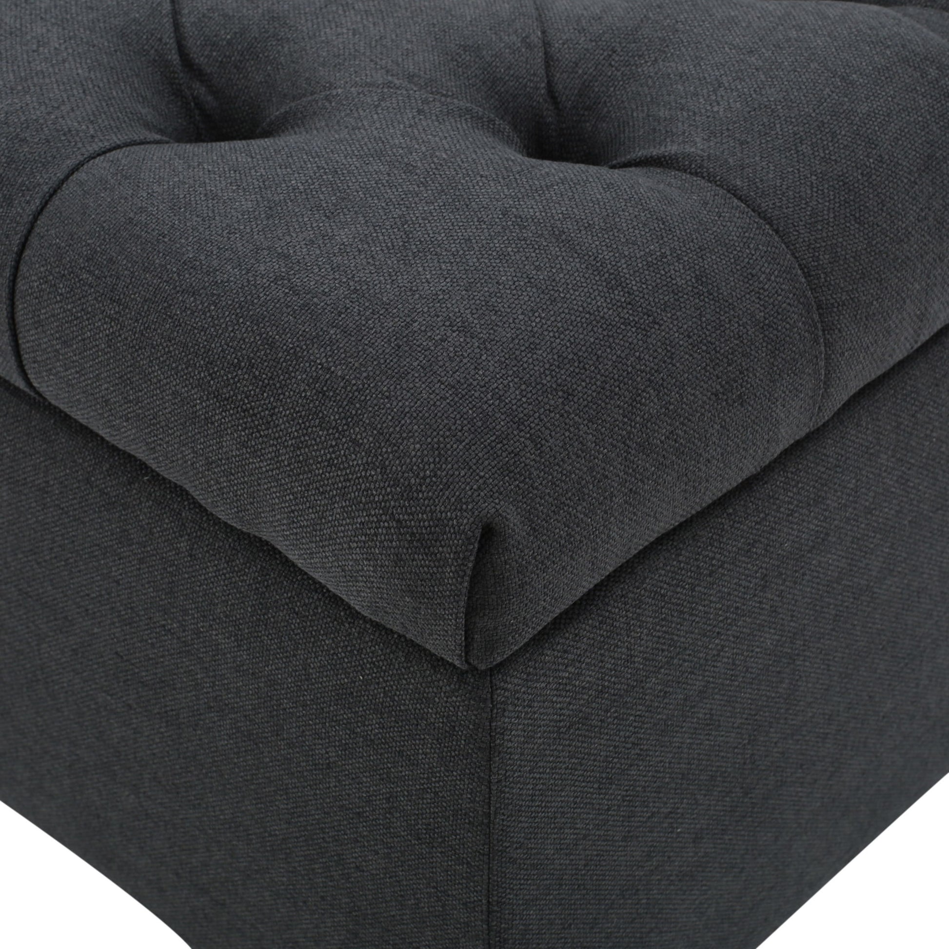 Close-up of the Glouster Contemporary Storage Ottoman, featuring dark grey fabric upholstery, visible stitching, and deep button tufted details.