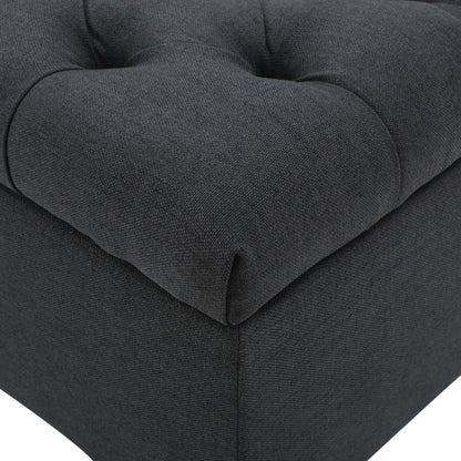 Close-up of the Glouster Contemporary Storage Ottoman, featuring dark grey fabric upholstery, visible stitching, and deep button tufted details.