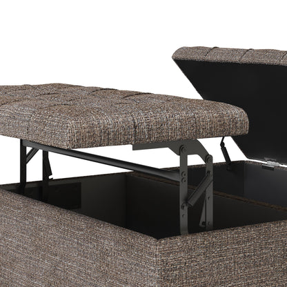 Close-up of the Harrison - Upholstered Coffee Table Storage Ottoman with its lid partially open, showing a metal hinge and empty compartment. Features textured brown and beige woven upholstery.
