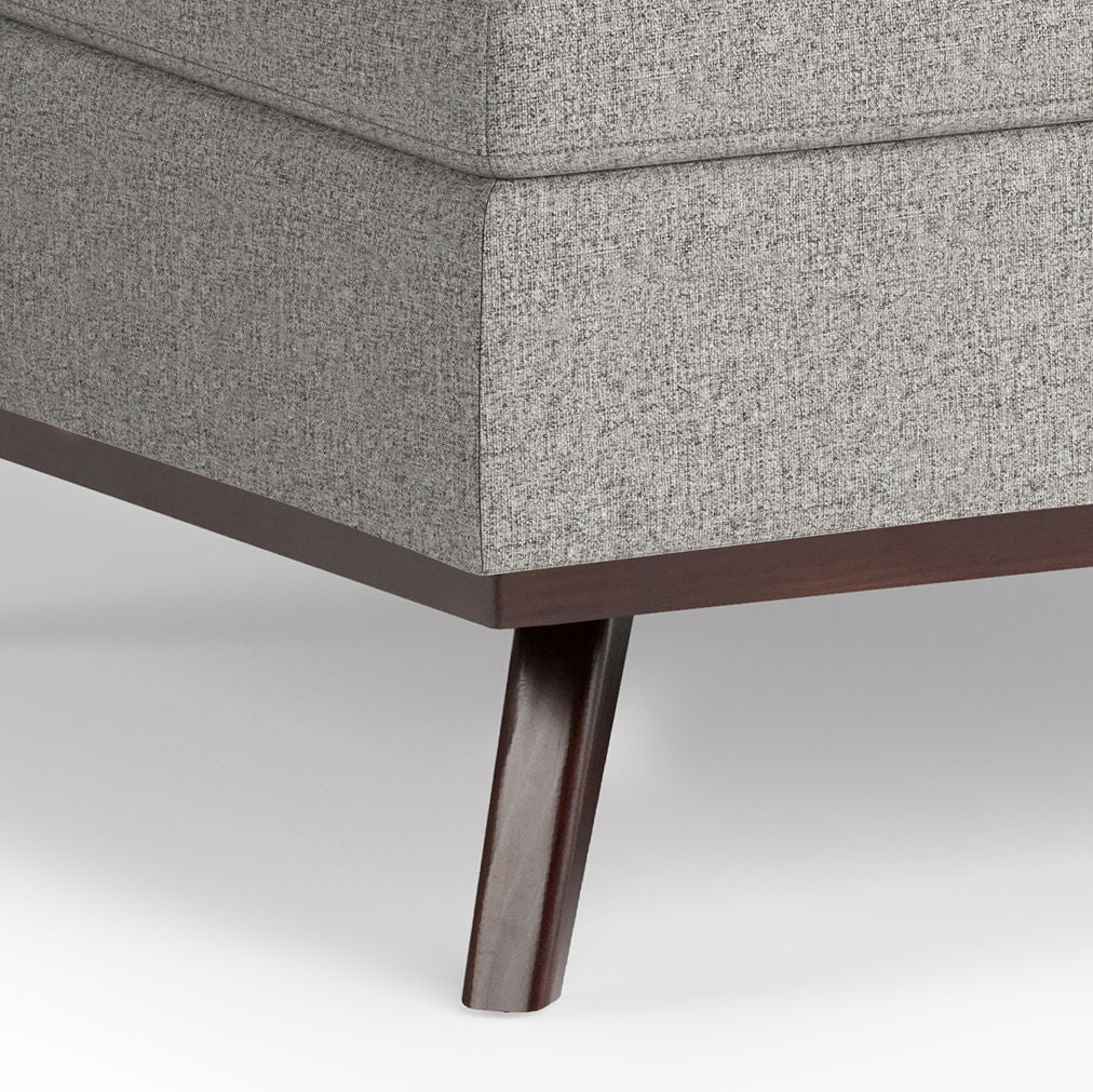 Close-up of the bottom corner of the Owen Multifunctional Square Coffee Table Storage Ottoman, featuring gray textured upholstery and a dark wooden leg on a white background.