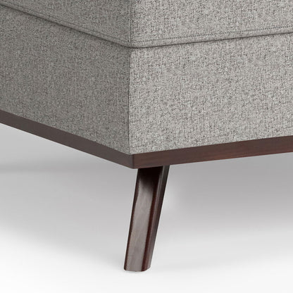 Close-up of the bottom corner of the Owen Multifunctional Square Coffee Table Storage Ottoman, featuring gray textured upholstery and a dark wooden leg on a white background.