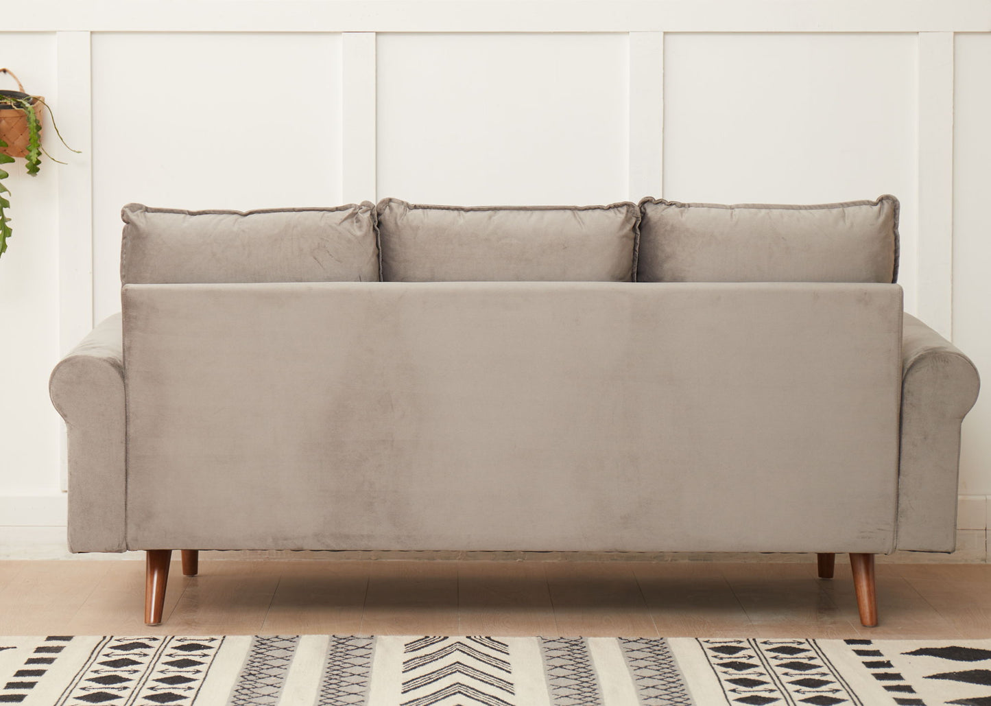 The Graceful Design Plush Comfort Sofa in light gray velvet, featuring three back cushions and wooden legs, sits against a white paneled wall with a black and white patterned rug partially visible on the floor.