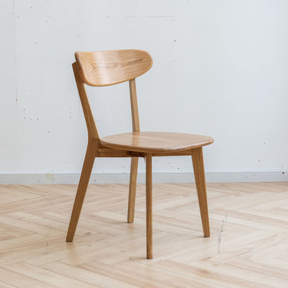 The Simple Dining Chair, Solid Chair Table for Living Room Chair features a minimalist wooden design with a curved backrest and round seat, shown on a light herringbone wooden floor against a plain white wall.