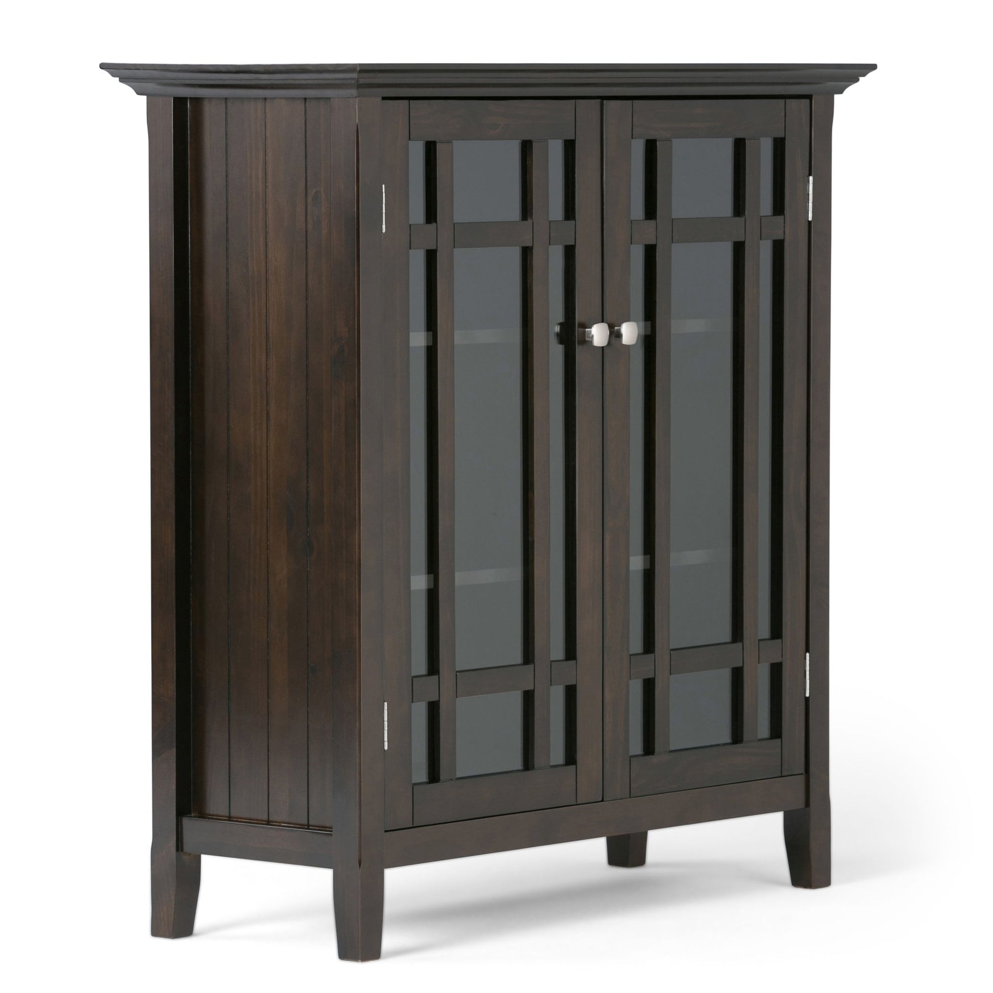 The Bedford Storage Media Cabinet features dark wood, glass-paneled double doors with a grid design, silver knobs, four legs, and a simple modern style. Interior shelves are visible through the glass.