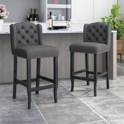 A pair of Vienna Contemporary Fabric Tufted Wingback Counter Stools in dark gray with nailhead trim are placed by a modern kitchen island with a marble countertop, gray tile flooring, and sleek contemporary decor.
