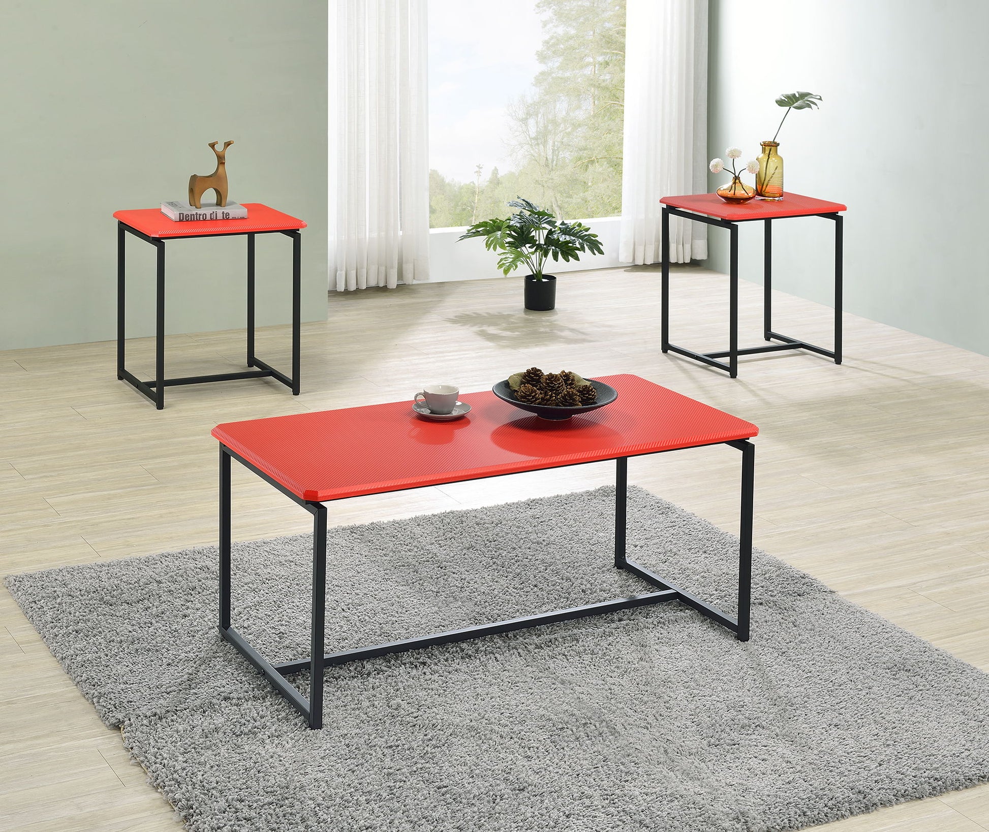 The GT - 3 Piece Carbon Fiber Wrap Coffee Table And End Table set features three modern tables arranged in a bright room with light wood floors, a gray rug, large windows, and adorned with decorative items and plants.